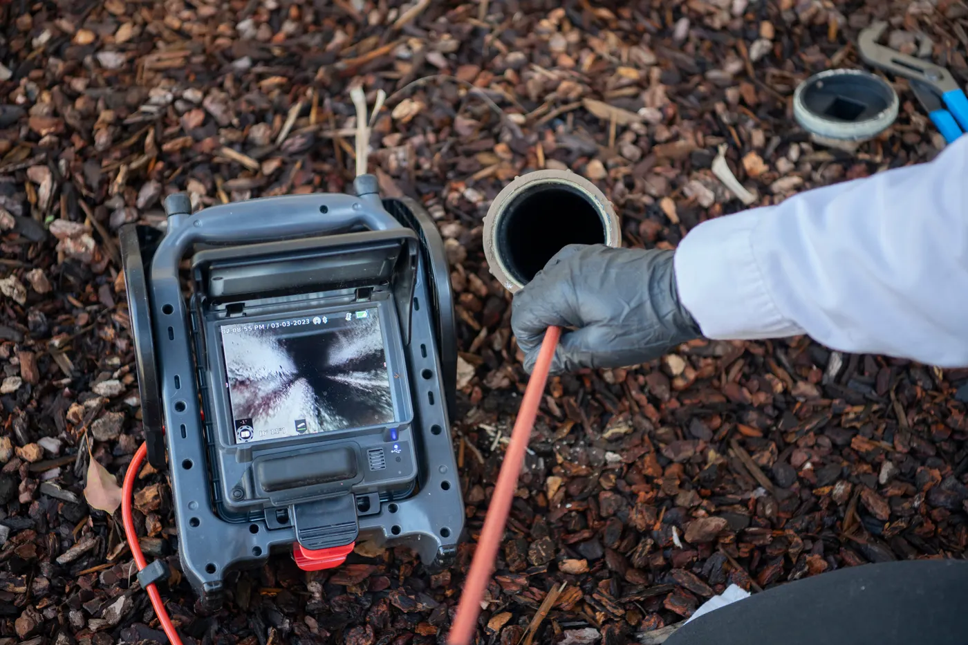 Sewer inspection camera monitor at a cleanout, with the scope line feeding down into the drain